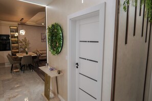 A modern interior with a white door, a small table with a decorative item, and a dining area with chairs and a table. - Designer Luxery 2 BR Apartment with Hot Mineral Water & Mineral Pool (VARNA)