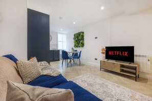 Una sala moderna con un sofá, una televisión y un comedor con sillas.