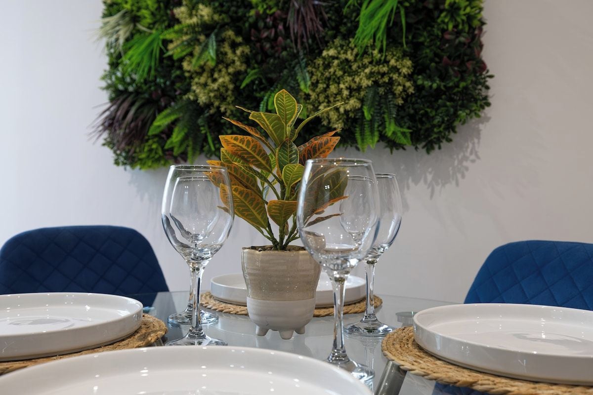 A dining table set with white plates, clear wine glasses, and a potted plant.