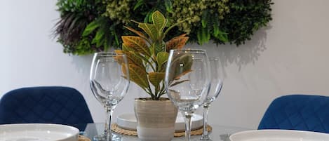 A dining table set with white plates, clear wine glasses, and a potted plant.