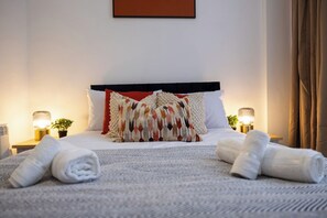 A neatly made bed with white linens and decorative pillows, two bedside lamps, and a small potted plant on a nightstand. - Central Brighton 2BR | Sleeps 4 | Near Seafront (Brighton and Hove)