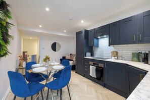 A modern kitchen with dark cabinets, a marble countertop, and a dining area with blue chairs. - Central Brighton 2BR | Sleeps 4 | Near Seafront (Brighton and Hove)