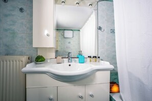 Ein Badezimmer mit einem weißen Waschbecken, einem Spiegel, einer kleinen Pflanze und Toilettenartikeln auf der Ablagefläche.