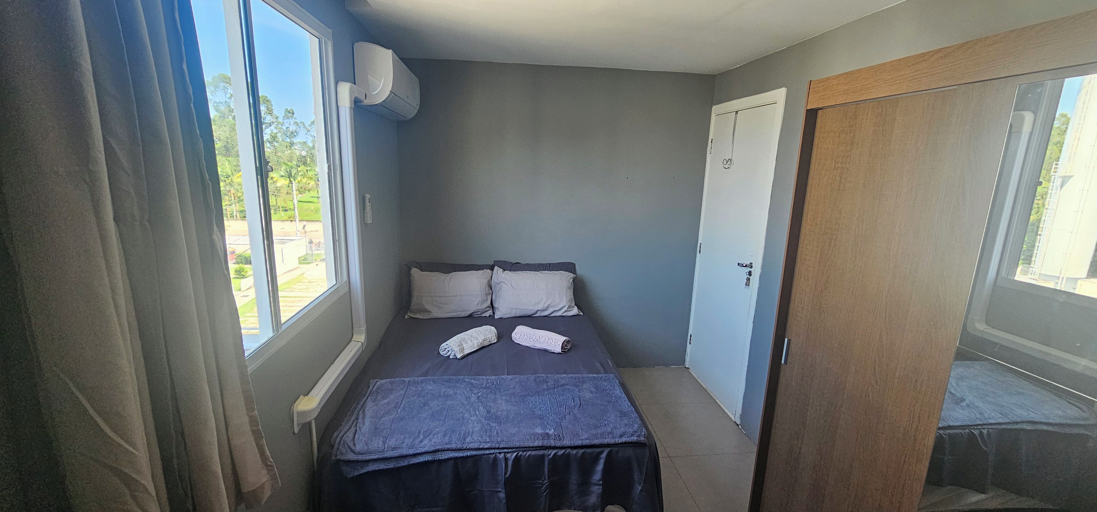 A small, narrow room with a bed, a window, and a door.