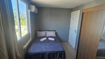 A small, narrow room with a bed, a window, and a door.