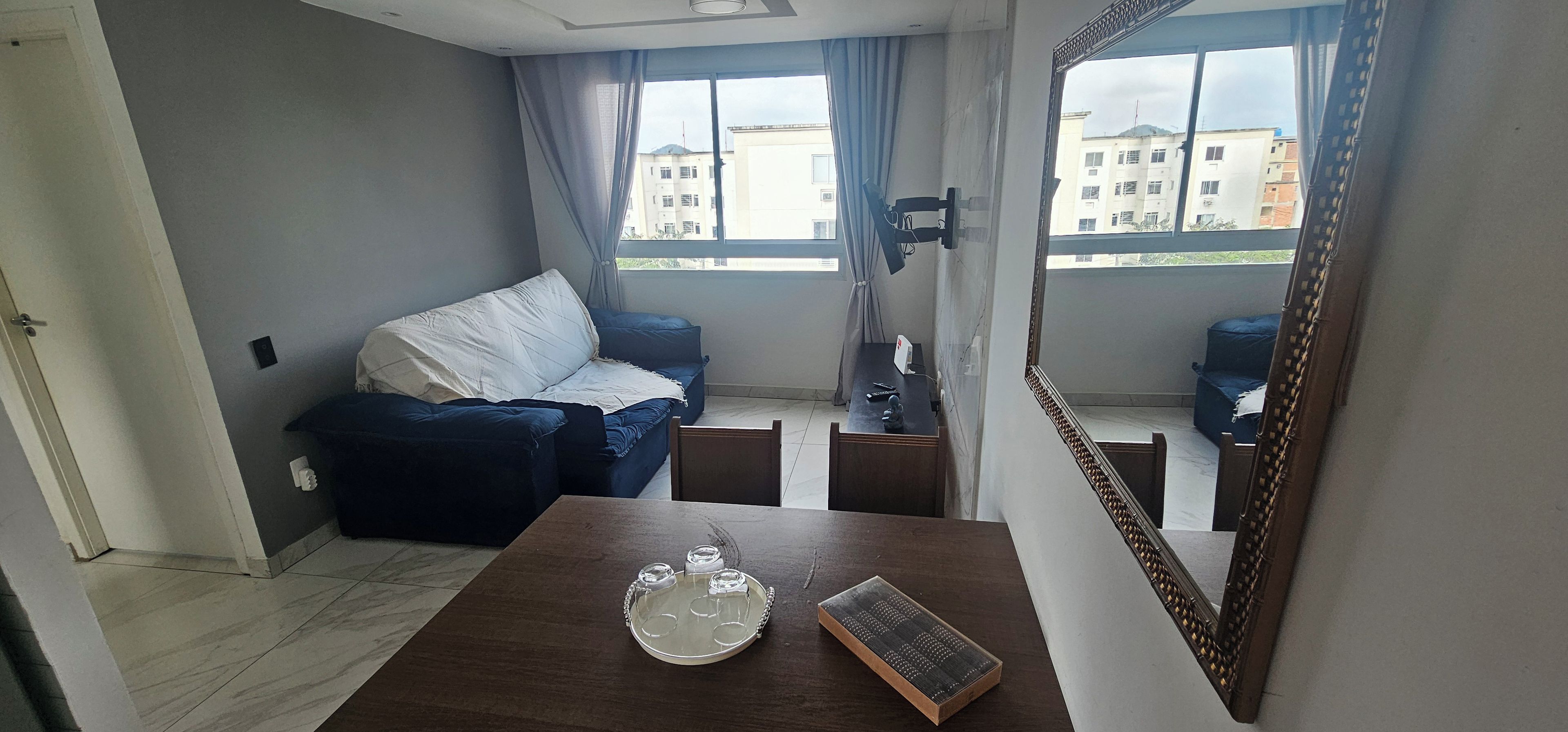 A room with a sofa, a dining table with a tray, and a large mirror.