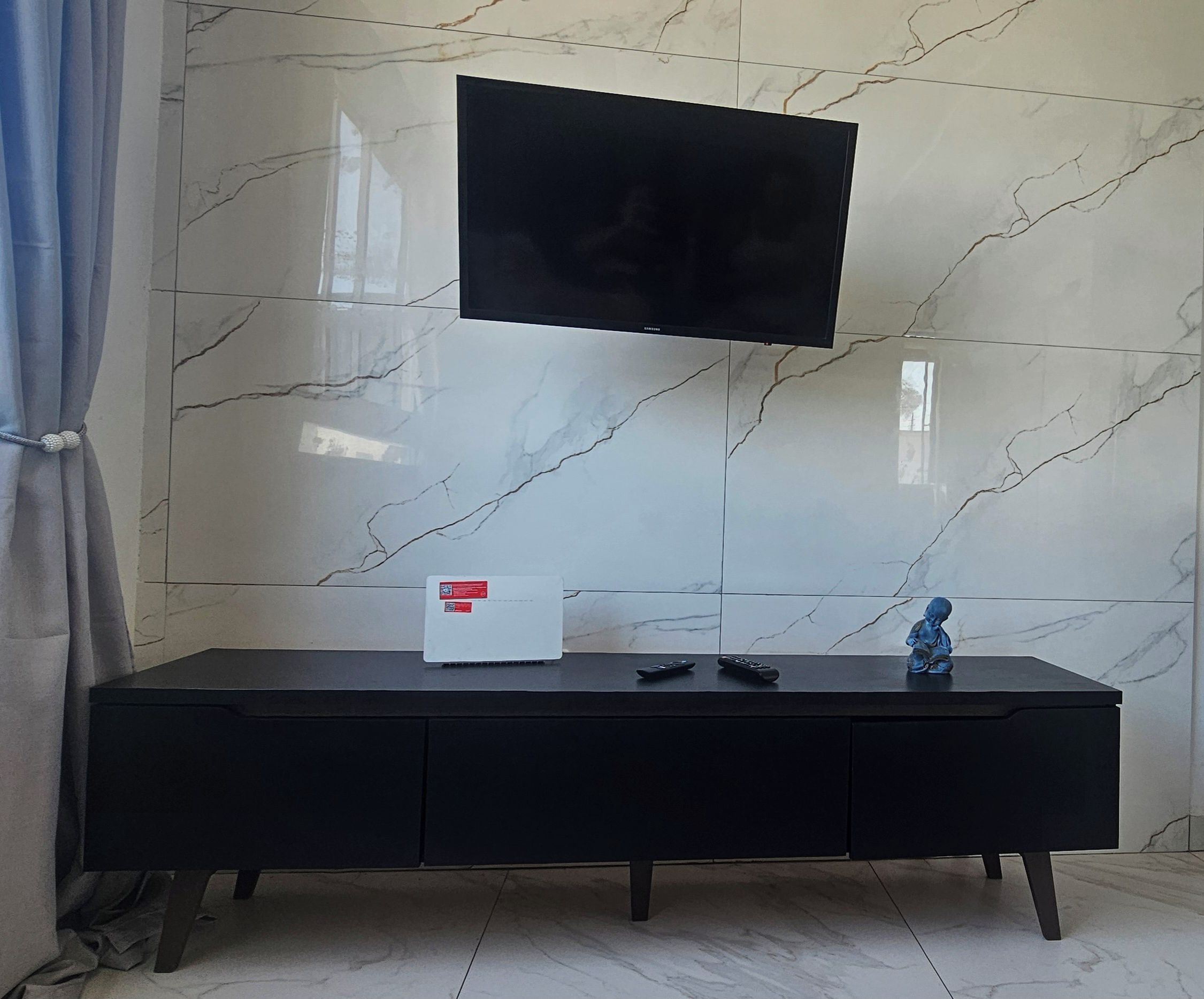 Un salon moderne avec un téléviseur à écran plat fixé à un mur en marbre, un meuble de rangement noir avec une télécommande et une petite figurine.