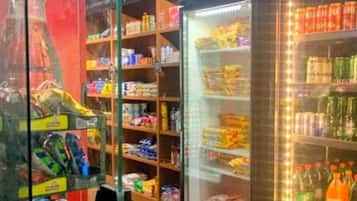 A refrigerated display area with snacks and beverages, shelves with packaged goods, and a glass door entrance.