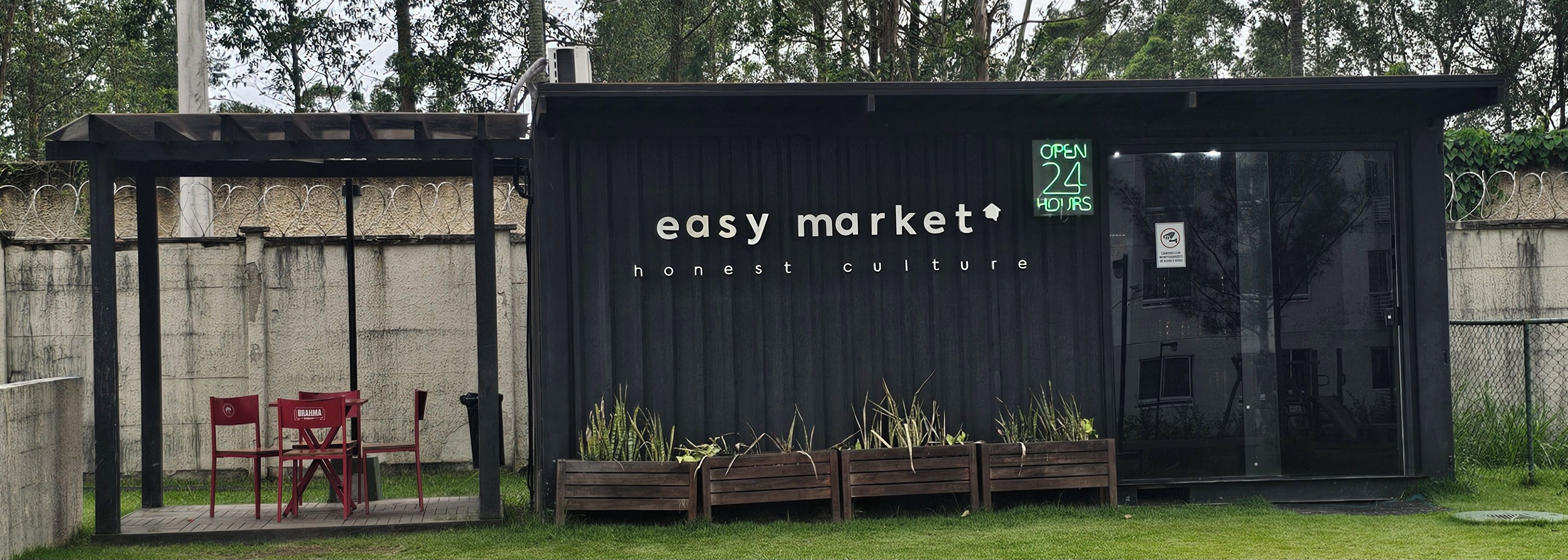 A small outdoor market with a sign that reads 'easy market honest culture' and a neon sign indicating 'OPEN 24 HOURS'.