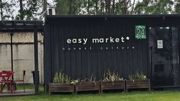 A small outdoor market with a sign that reads 'easy market honest culture' and a neon sign indicating 'OPEN 24 HOURS'.