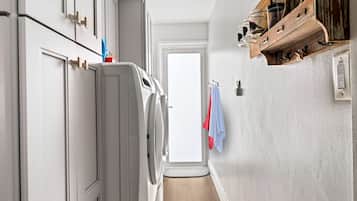 A laundry room with a washing machine, a dryer, and a wooden shelf with jars.