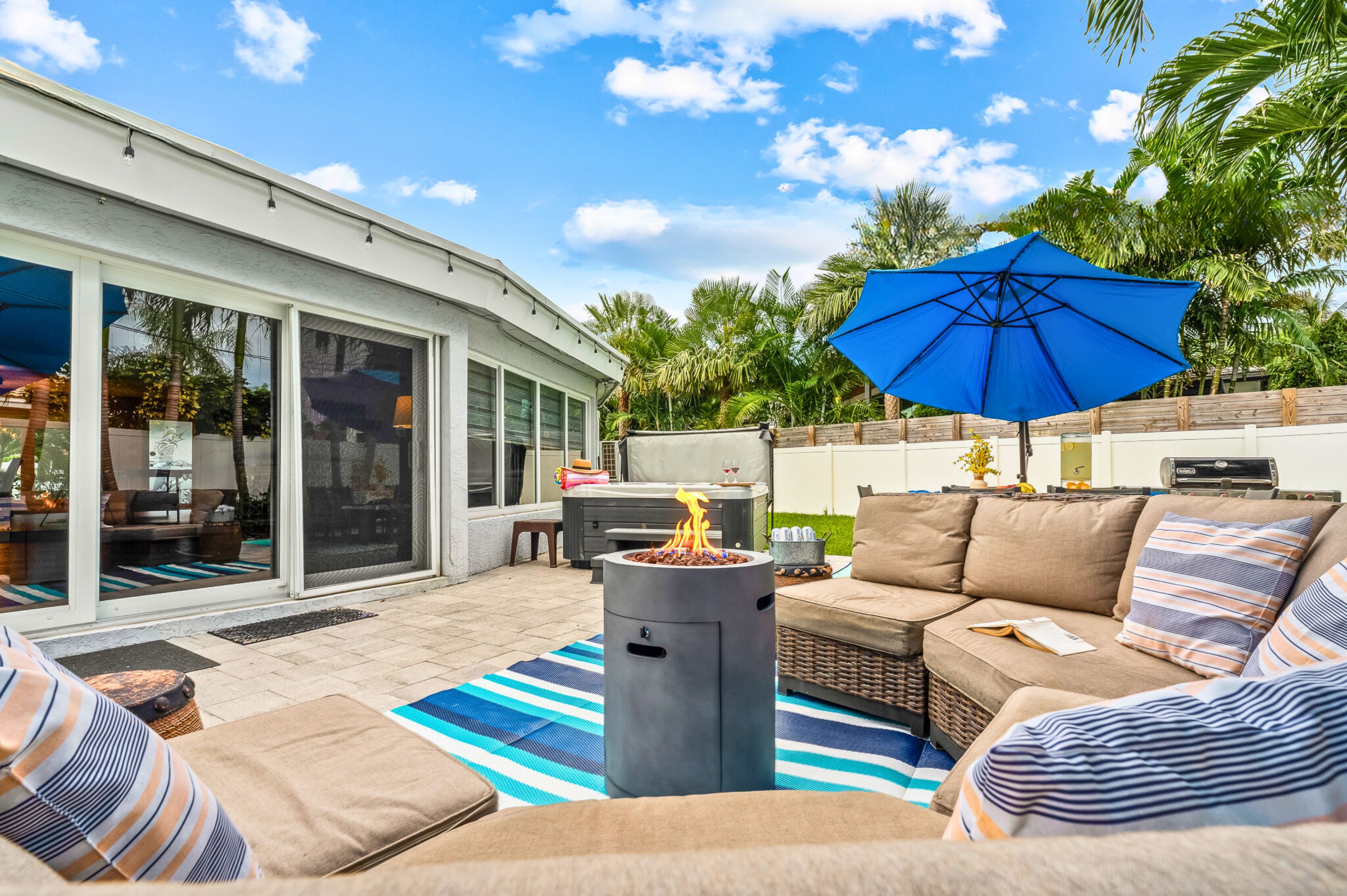 Une terrasse avec un foyer extérieur, des meubles de jardin et un parasol bleu.