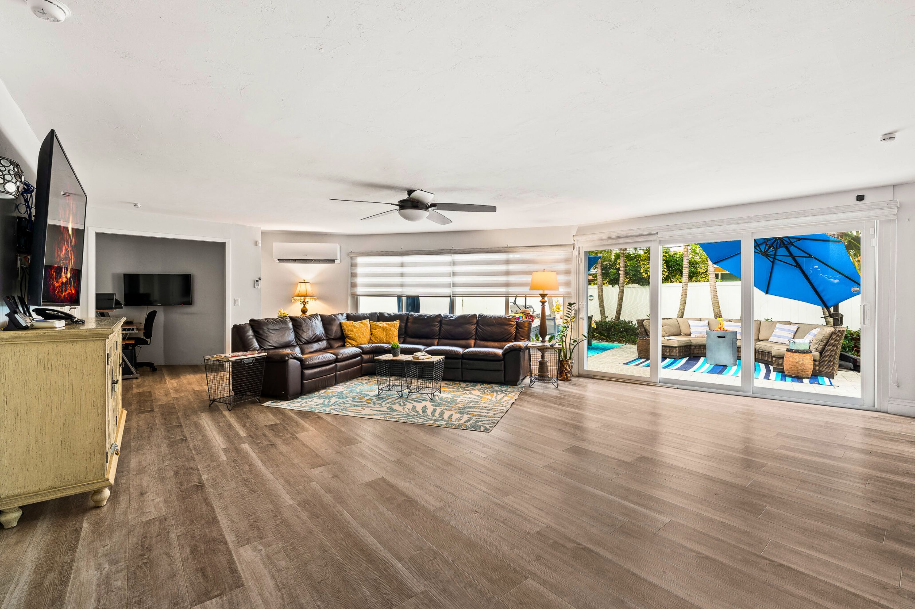 A spacious living room with a sectional sofa, a coffee table, and a television. There is a sliding glass door leading to an outdoor area with a patio set.