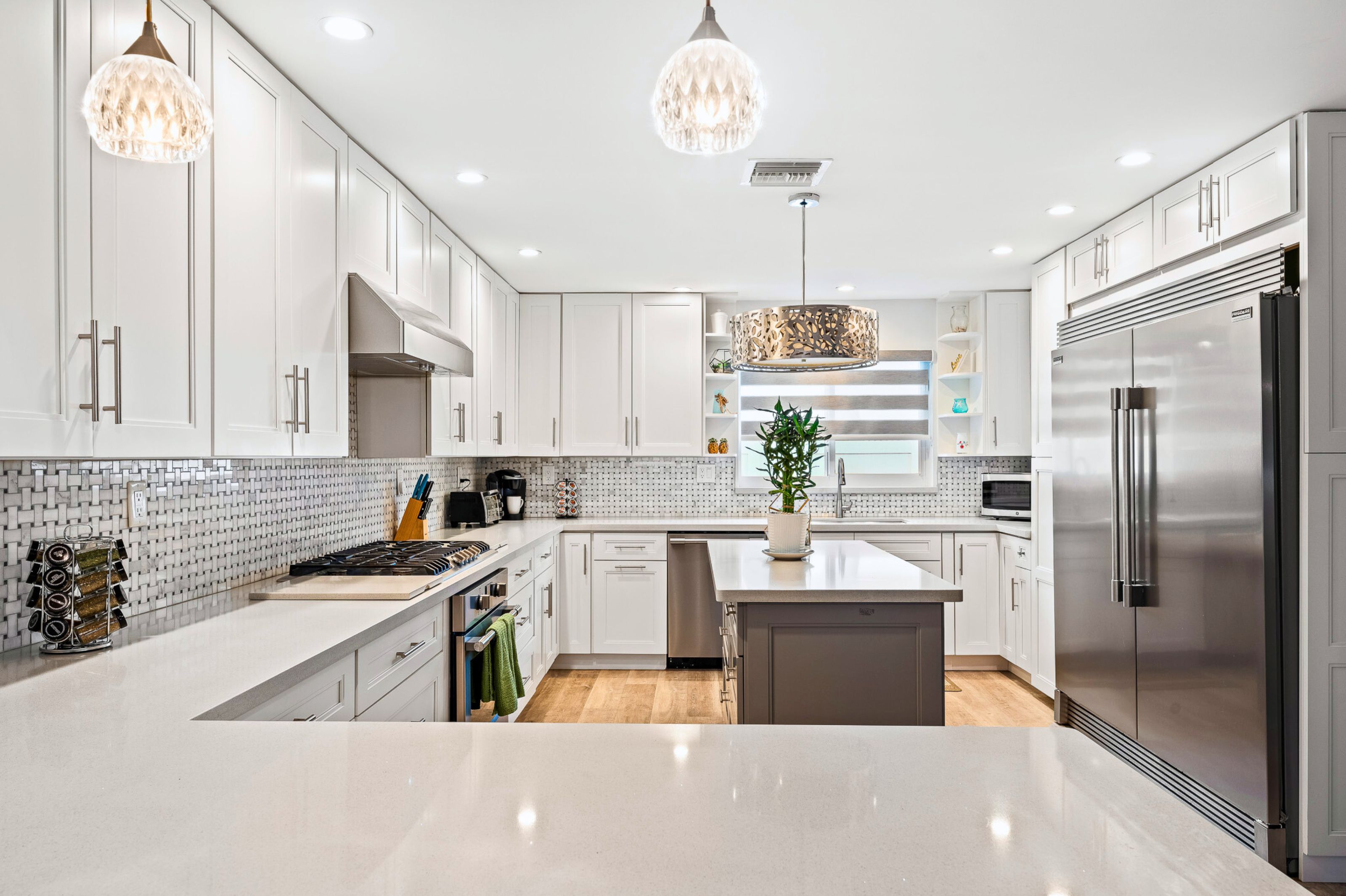Une cuisine moderne avec des meubles blancs, des appareils en acier inoxydable et des luminaires suspendus.