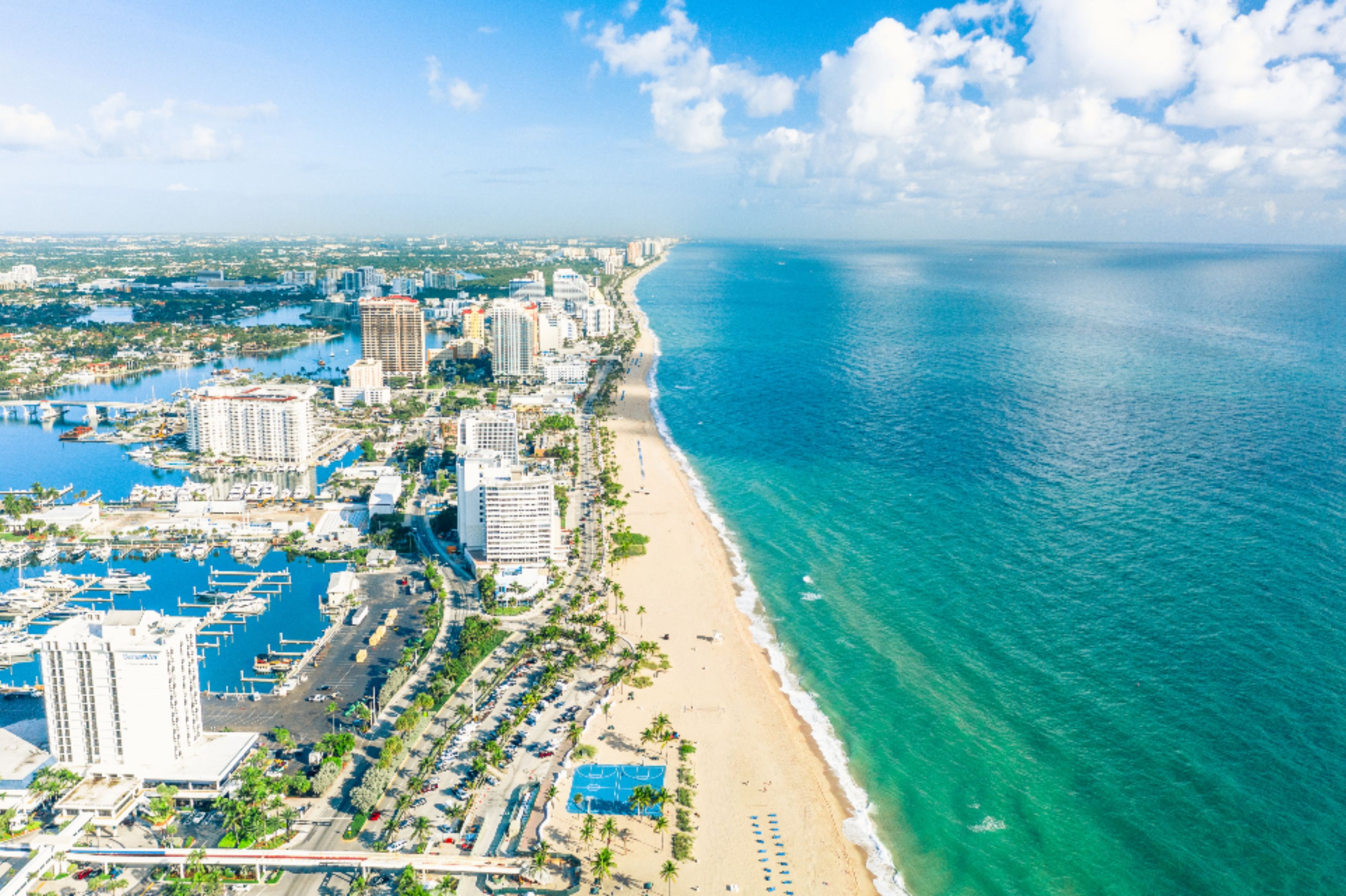 A coastal cityscape with a marina, high-rise buildings, and a beach.
