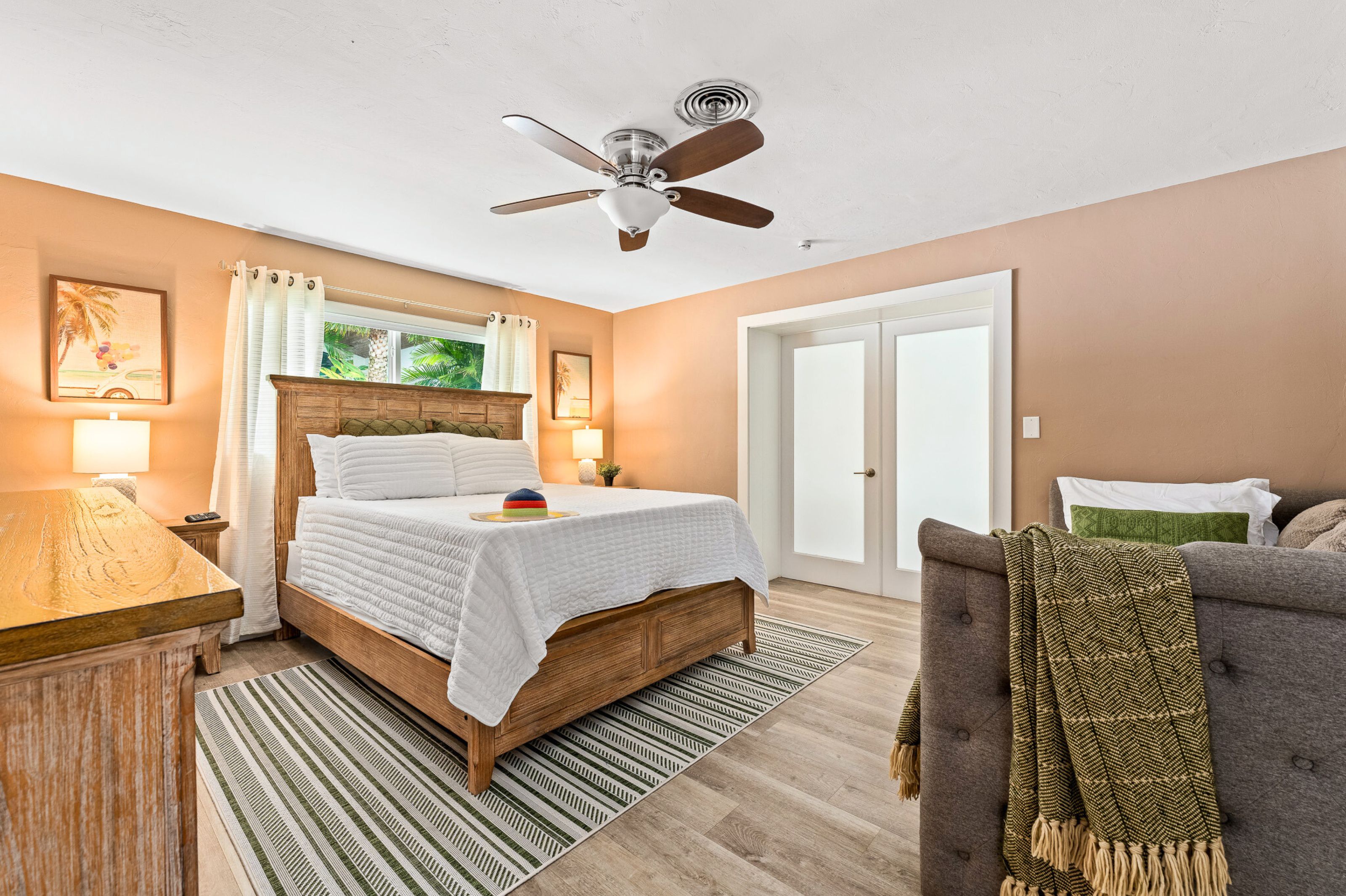 A bedroom with a bed, a ceiling fan, a window with curtains, a bedside table, and a chair.