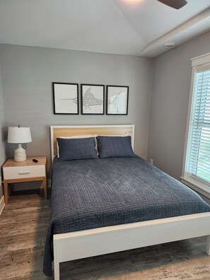 Une chambre à coucher avec un lit, une table de chevet, une lampe et trois tableaux encadrés accrochés au mur.