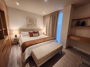 Ein modernes Schlafzimmer mit einem großen Bett, Nachttischlampen, einem Kopfteil mit ungewöhnlichem Design, einer Sitzbank am Fußende des Bettes und einem Regal mit Dekorationen.