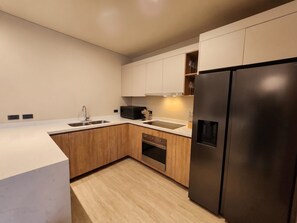 A modern kitchen with a stainless steel refrigerator, wooden cabinets, a double sink, and a microwave. - Ameth: Bright 2BR in Downtown with Rooftop Pool (Cabo San Lucas)