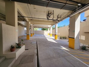 A covered parking area with concrete pillars, potted plants, and clear signage. - Ameth: Bright 2BR in Downtown with Rooftop Pool (Cabo San Lucas)