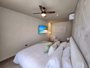 Une chambre d’hôtel avec un lit, un ventilateur de plafond, un téléviseur fixé au mur et une table de chevet avec une lampe.