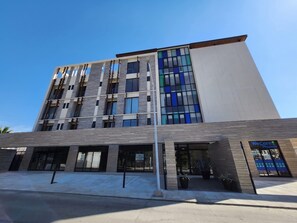 A modern building with a flat roof, large windows, and a sign for WeCare Pharma. - Ameth: Bright 2BR in Downtown with Rooftop Pool (Cabo San Lucas)
