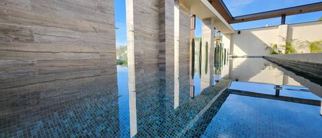 Un edificio moderno con zona de piscina, destacando un suelo de vidrio transparente y vistas al cielo.