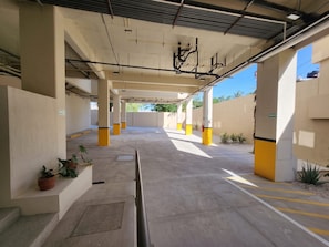 A covered parking area with concrete pillars, potted plants, and clear signage. - Ameth: Stylish 3BR in Downtown with Rooftop Pool (Cabo San Lucas)