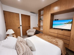 A hotel room with a bed, a chair, a TV, and wooden storage units. - Ameth: Stylish 3BR in Downtown with Rooftop Pool (Cabo San Lucas)
