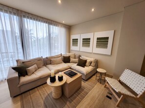 A modern living room with a sectional sofa, a coffee table, and a small side table. There are three wall-mounted artworks and a woven rug on the floor. - Ameth: Spacious 3BR Apartment with Rooftop Pool (Cabo San Lucas)