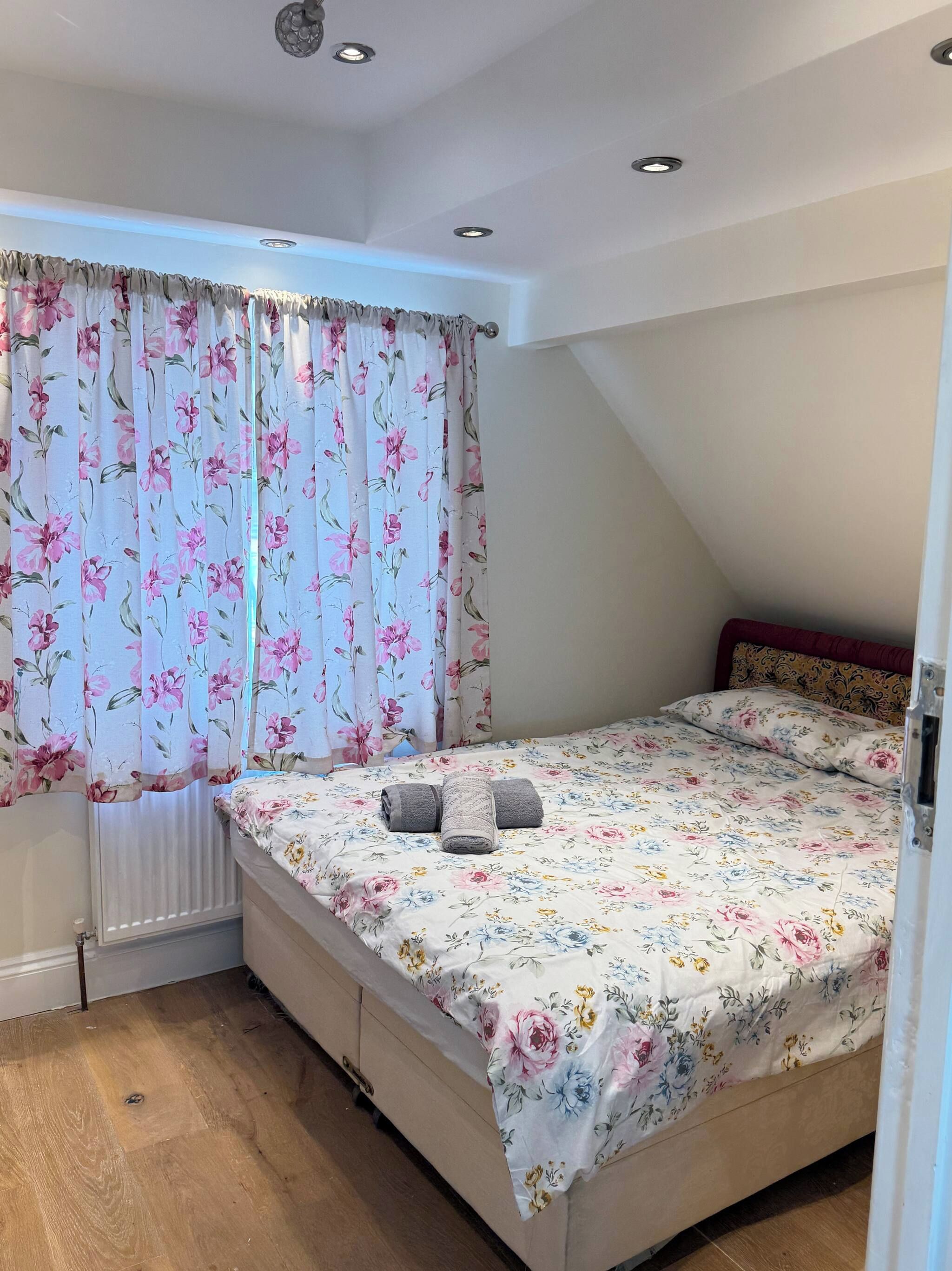 Ein Schlafzimmer mit einem Bett, einem Heizkörper und einem Fenster mit blumigen Vorhängen.