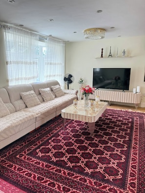 Una sala de estar con un sofá, una mesa de centro, un televisor y una alfombra estampada.