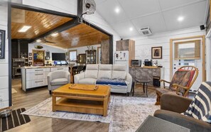 A spacious living area with a wooden ceiling, a sofa, a coffee table, and a kitchen in the background. - Cottage with attached Tiny house, close to lakes (Westree)