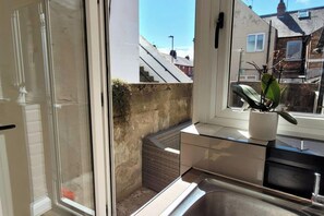 Ett modernt kök med en inbyggd diskho, ett fönster med utsikt över ett bostadsområde och en krukväxt på bänkskivan.