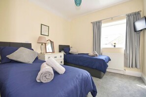 A hotel room with two beds, a TV, a window with curtains, and a radiator. - Sea Escape - Convenient location (North Yorkshire)