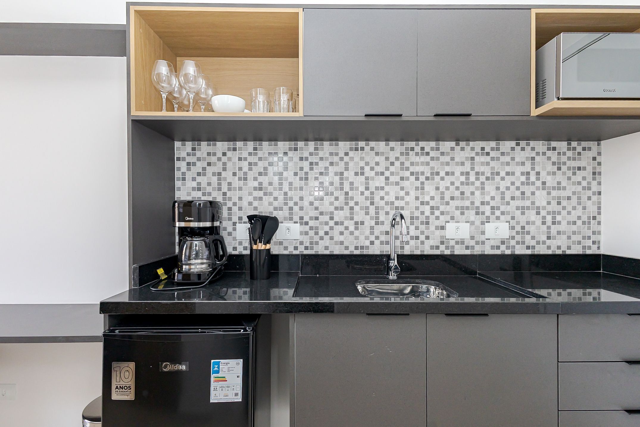 A modern kitchen with a black countertop, a coffee maker, a sink, and a tiled backsplash.