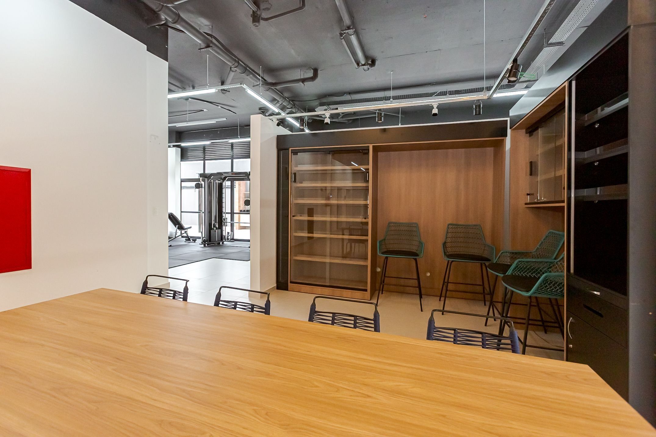 Un salón de conferencias con una mesa y sillas de madera, un separador de vidrio con una estantería, y una pared de acento roja.