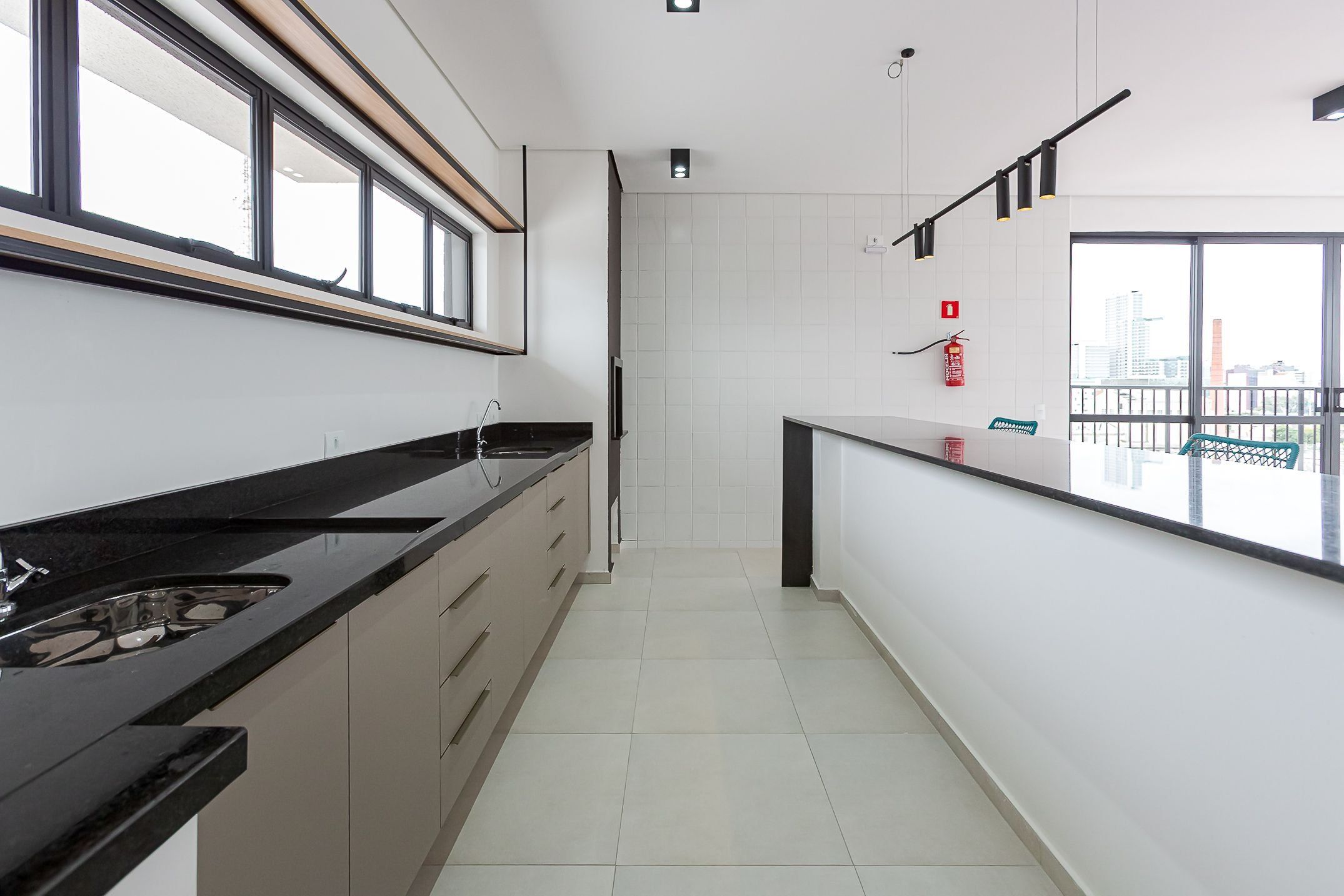 Cozinha moderna com bancada ampla, armários e vista para a cidade através de grandes janelas.
