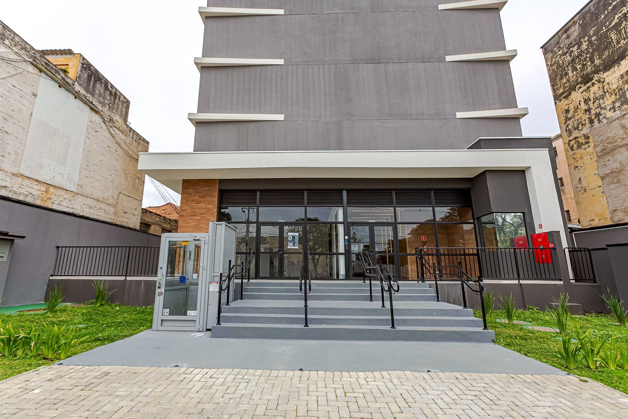 Un bâtiment moderne doté d’une entrée en verre, d’un escalier menant à l’entrée et d’un trottoir dallé.