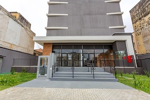 Un edificio moderno con entrada de vidrio, una escalera que conduce a la entrada y un camino pavimentado.