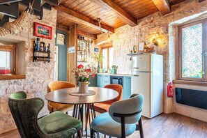 Een landelijke keuken met stenen muren, houten balkenplafond, een ronde eettafel met stoelen en een koelkast.