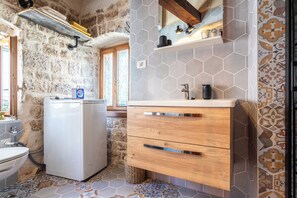 Een kleine keuken met een wasmachine, houten kastjes en een achterwand van honingraatmozaïek.