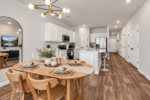 Une cuisine moderne avec des meubles blancs, un îlot central et un coin repas agrémenté d’une table en bois, mise pour quatre personnes.