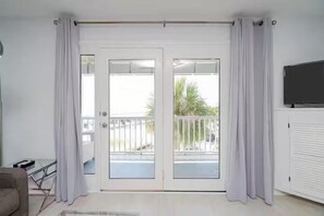 Ein Zimmer mit einer Schiebeglastür, die auf einen Balkon führt, einem an der Wand montierten Fernseher und einem Heizkörper.
