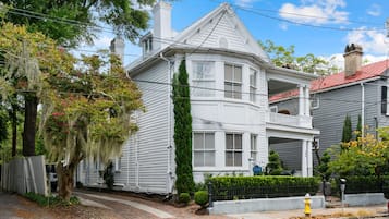 Une maison blanche à deux étages, dotée d’un porche, d’une cheminée et d’un toit rouge.