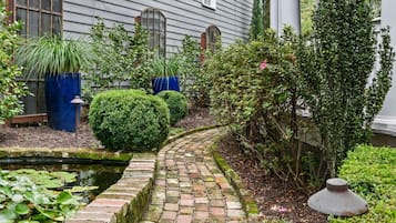 A brick pathway leading to a house with a covered porch and a small pond with lily pads.
