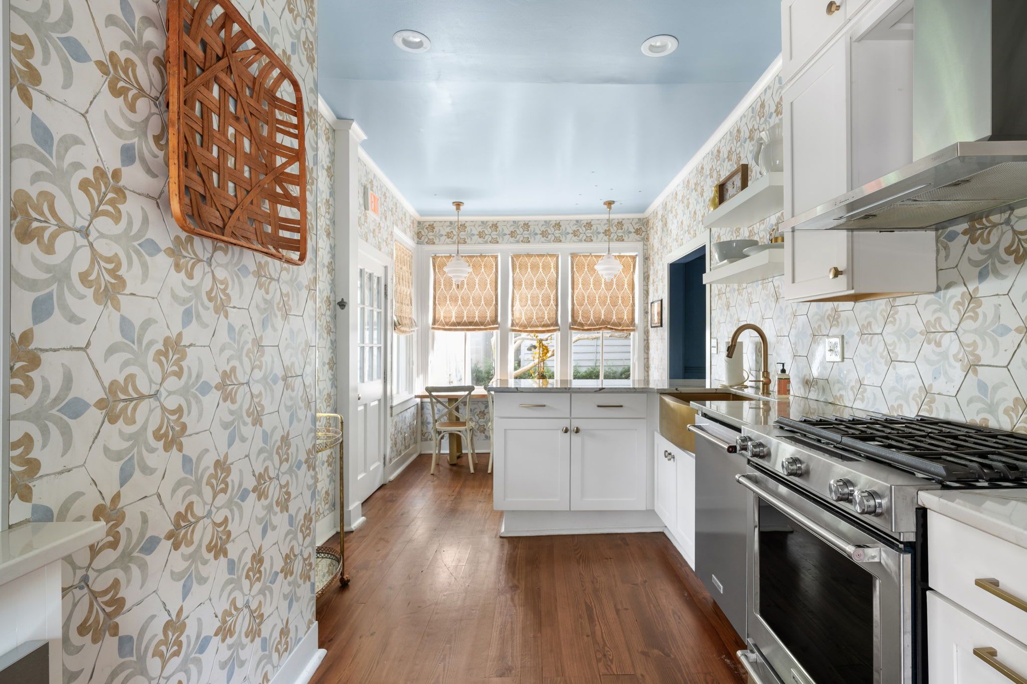 A kitchen with white cabinets, a stainless steel stove, and patterned wallpaper.