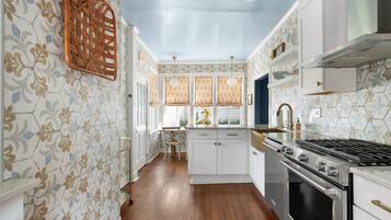 A kitchen with white cabinets, a stainless steel stove, and patterned wallpaper.