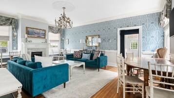 A spacious living room with a fireplace, teal sofas, and a dining area with a wooden table and chairs.