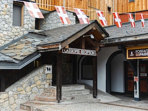 A reception area with a stone facade, wooden beams, and a sign indicating a ski pass service. - Cozy apartment near the slopes - 4 guests (Belle Plagne)